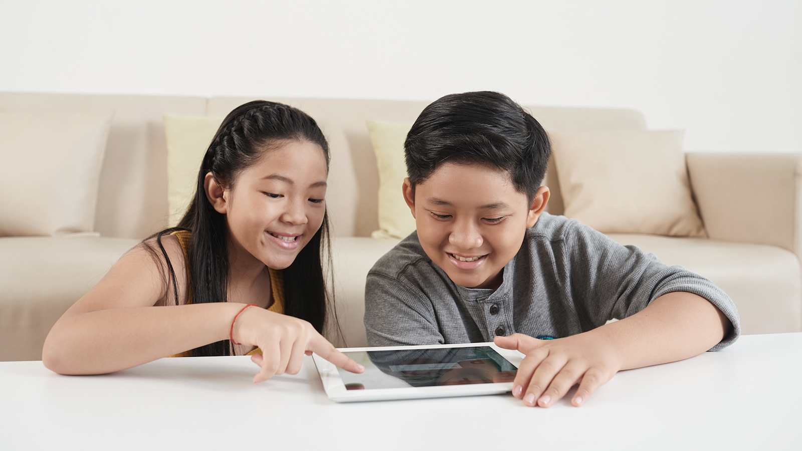 Asian siblings playing game on digital tablet at home